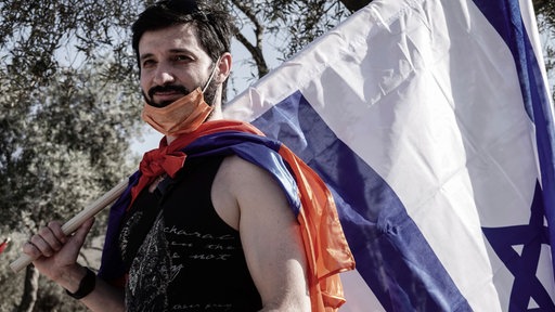 Das Bild zeigt einen armenischen Bewohner Jerusalems mit einer Fahne Armeniens und einer israelischen Fahne. Das Foto ist 2020 bei Protesten in Jerusalem im Kontext des armenisch-aserbaidschanischen Konflikts um Berg-Karabach entstanden. 