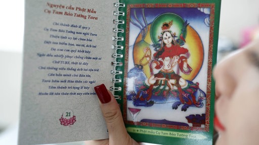 Eine Buddhistin betrachtet ein Buch mir der Abbildung der Tara.