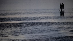 Ein Paar geht durch das Watt - sie sind nur als Silhouette erkennbar
