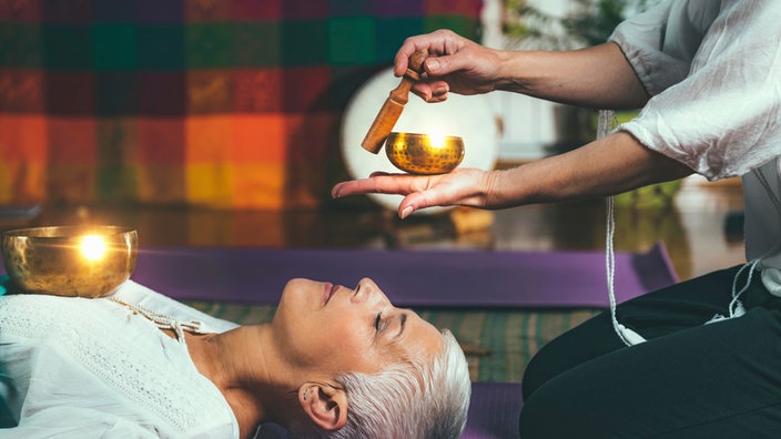 Eine Frau liegt bei einer Klangschalentherapie entspannt auf dem Boden