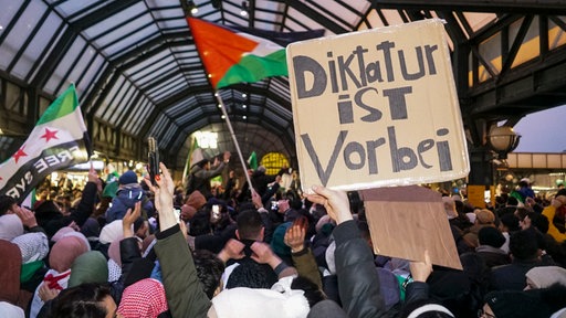 Syrische Geflüchtete in Deutschland feiern am 8. Dezember 2024 im Hamburger Hauptbahnhof das Ende der Assad-Diktatur. Auf einem Plakat steht geschrieben: Diktatur ist vorbei