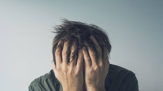 Ein Mann sitzt traurig am Boden und bedeckt sein Gesicht mit den Händen