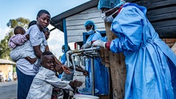 Eine Mutter und ihre Kinder waschen sich an einem Gesundheitscheckpoint in Goma, Kongo, die Hände an einer provisorischen Waschstation.