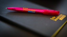 Ein pinker Kugelschreiber mit dem FDP-Schriftzug liegt auf einem schwarzen Notizbuch.