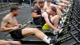 Teilnehmer rudern bei einem HYDROX-Wettbewerb an Rudermaschinen auf der Fitnessmesse "Fibo 2025"