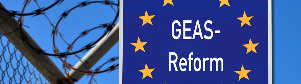 Fotomontage: Neben einem Zaun mit Natodraht steht ein blaues Schild mit Europasternen, auf dem "GEAS-Reform" zu lesen ist.