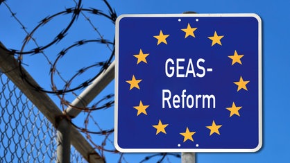 Fotomontage: Neben einem Zaun mit Natodraht steht ein blaues Schild mit Europasternen, auf dem "GEAS-Reform" zu lesen ist.