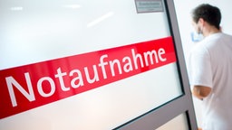 Ein Krankenpfleger steht neben einer Glastür mit der Aufschrift "Notaufnahme"