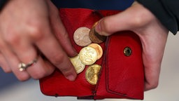 Nahaufnahme der Hände: Eine Person zählt Münzen in einem roten Portemonnaie.