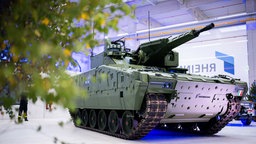 Ein Panzer steht in einer Ausstellungshalle. Im Hintergrund ist der Schriftzug "Rheinmetall" zu sehen.