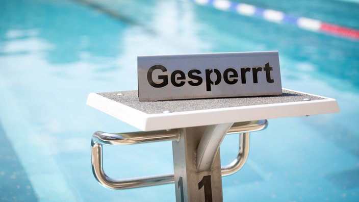 "Gesperrt" ist auf einem Schild zu lesen, das auf dem Startblock in einem geschlossenen Freibad steht.