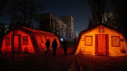 Menschen gehen an Notzelten vorbei, die in Kiew, Ukraine, zum Aufwärmen aufgestellt wurden.