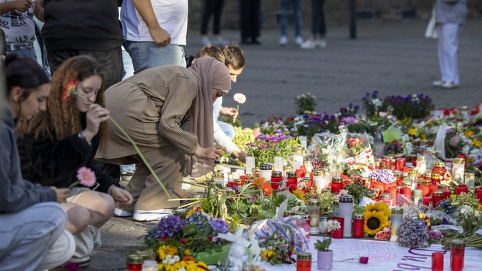 Menschen legen in der Nähe des Tatorts der Messerattacke auf dem Solinger Stadtfest Blumen und Kerzen zum Gedenken der Opfer nieder. 