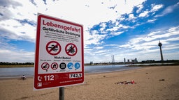 Ein Hinweisschild am Paradiesstand in Düsseldorf weist auf die Gefahren beim Schwimmen im Rhein hin