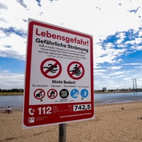 Ein Hinweisschild am Paradiesstand in Düsseldorf weist auf die Gefahren beim Schwimmen im Rhein hin