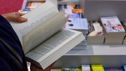 Symbolbild: Ein Mensch blättert in einem Buchladen in einem Buch.