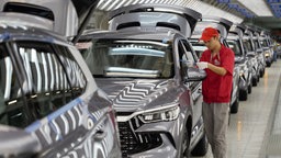 Ein Mitarbeiter im Werk des chinesischen Autoherstellers BYD entfernt Schutz-Klebefolie von einer Reihe Fahrzeuge.