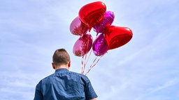 Symbolbild: Ein junger Mensch mit Herz-Luftballons.