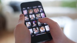 Symbolbild (anonymisiert/Rauschfilter): Ein Mensch schaut sich auf einem Smartphone Profilbilder auf einer Internet-Pornoseite an.