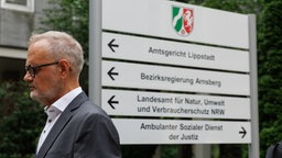 Gynäkologe Dr. Volz vor Wegweisern vor dem Amtsgericht in Lippstadt