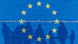 Europaflagge auf einer Mauer und Umrisse von Asylsuchenden hinter einem Stacheldraht. Symbolbild Asylrechtsreform
