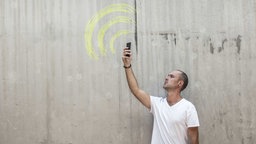 Symbolbild: Ein Mensch hält ein Smartphone auf der Suche nach einer guten Verbindung nach oben.