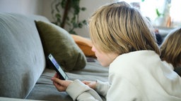 Symbolbild: Kind mit Smartphone auf einem Sofa.