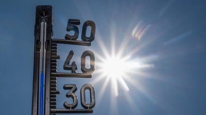 Ein Thermometer zeigt heiße Temperaturen an, im Hintergrund die gleißende Sonne