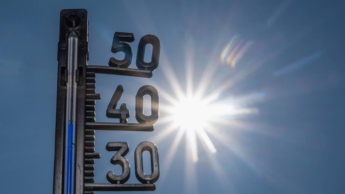 Ein Thermometer zeigt heiße Temperaturen an, im Hintergrund die gleißende Sonne