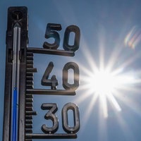 Ein Thermometer zeigt heiße Temperaturen an, im Hintergrund die gleißende Sonne