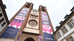Banner des Deutschen Katholikentages 2026 mit der Aufschrift "Steh auf" und "Hab Mut" in Würzburg an einer Kirche.