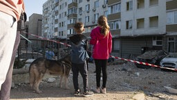 Ukrainische Kinder blicken auf ein beschädigtes Gebäude nach einem russischen Luftangriff. 