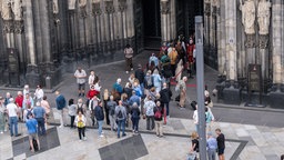 Besucher stehen vor dem Dom in Köln und warten auf den Einlass. 