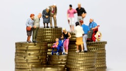 Symbolbild: Miniatur Figuren aller Altersgruppen stehen auf Münzstapeln
