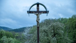Symbolbild: Kreuz mit Jesus in einer Waldlandschaft.