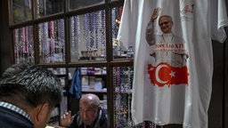 Symbolbild: In einem Ladenfenster hängt ein T-Shirt, bedruckt mit einem Bild von Papst Leo und der türkischen Flagge.