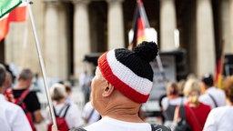 Reichsbürger demonstrieren am 31.08.2024 in München. Mann im Vordergrund trägt eine schwarz-weiß-rote Strickmütze.