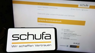 Symbolbild: Ein Smartphone-Display und ein Monitor zeigen den Web-Auftritt der Schufa.