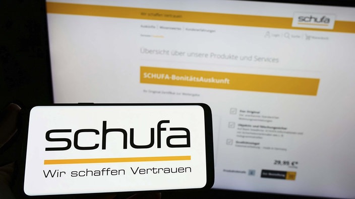 Symbolbild: Ein Smartphone-Display und ein Monitor zeigen den Web-Auftritt der Schufa.