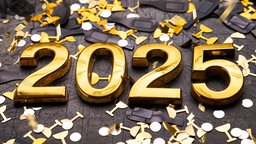 Eine goldene 2025 liegt zwischen Konfetti in schwarz und gold.