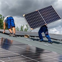 Symbolbild: Zwei Menschen decken ein Dach mit Solarmodulen