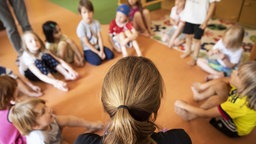 Symbolbild: Eine Erwachsene in einem Kreis von Kindern, die zuhören.