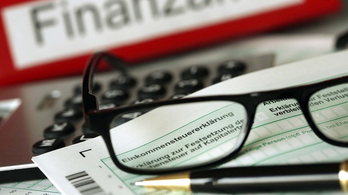 Ordner mit der Aufschrift "Finanzamt" und auf einem Vordruck für die Steuererklärung liegen Stift und Brille.