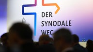 Teilnehmer der Synodalversammlung sitzen vor dem Schriftzug "Der Synodale Weg". 