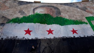  Ein syrischer Junge steht unter einem riesigen Porträt des verstorbenen syrischen Präsidenten Al-Assad, übermalt mit den Farben der sogenannten "revolutionären" Flagge.