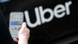 Symbolbild: Uber-App auf einem Smartphone-Display neben dem Schriftzug "Uber".