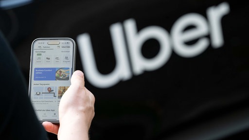 Symbolbild: Uber-App auf einem Smartphone-Display neben dem Schriftzug "Uber".