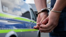 Symbolbild: Eine Person mit Handschellen vor einem Polizeiauto