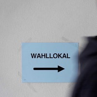 Ein junger Mann läuft an Schild mit der Aufschrift "Wahllokal" vorbei