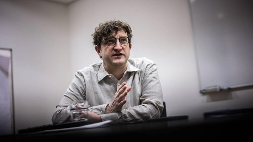 Das Foto von Andreas Stahl zeigt ihn sitzend an einem Tisch: mit kurzem lockigem Haar, dunkler Brille und hellem Hemd.